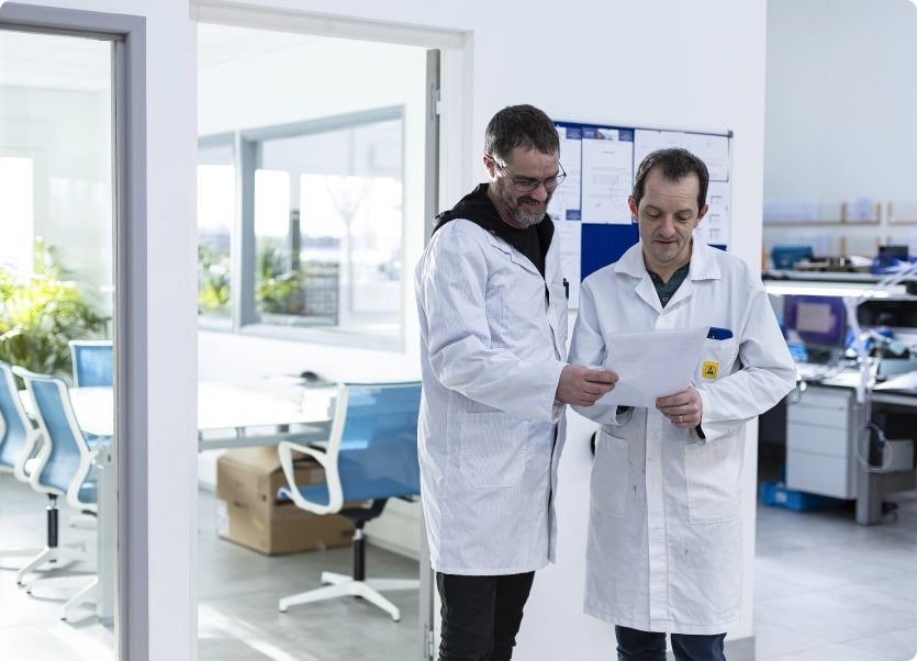Deux experts en réparation électronique discutent d’un diagramme technique dans un cadre de travail chaleureux.
